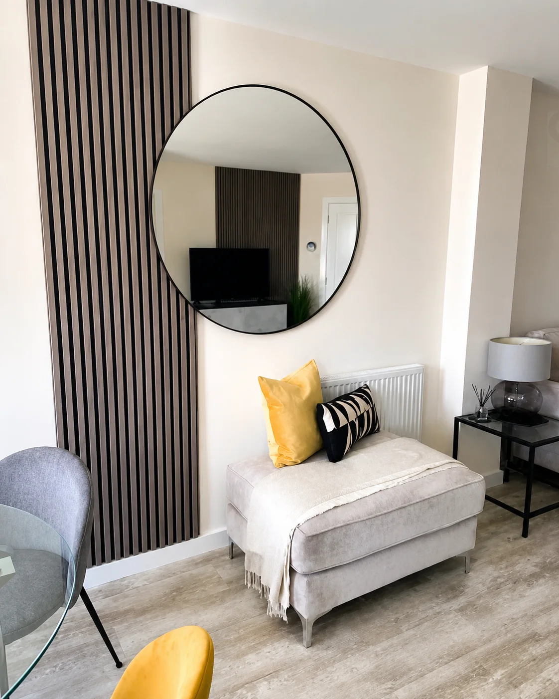 Dark slat wall beside a round mirror and lounge chair